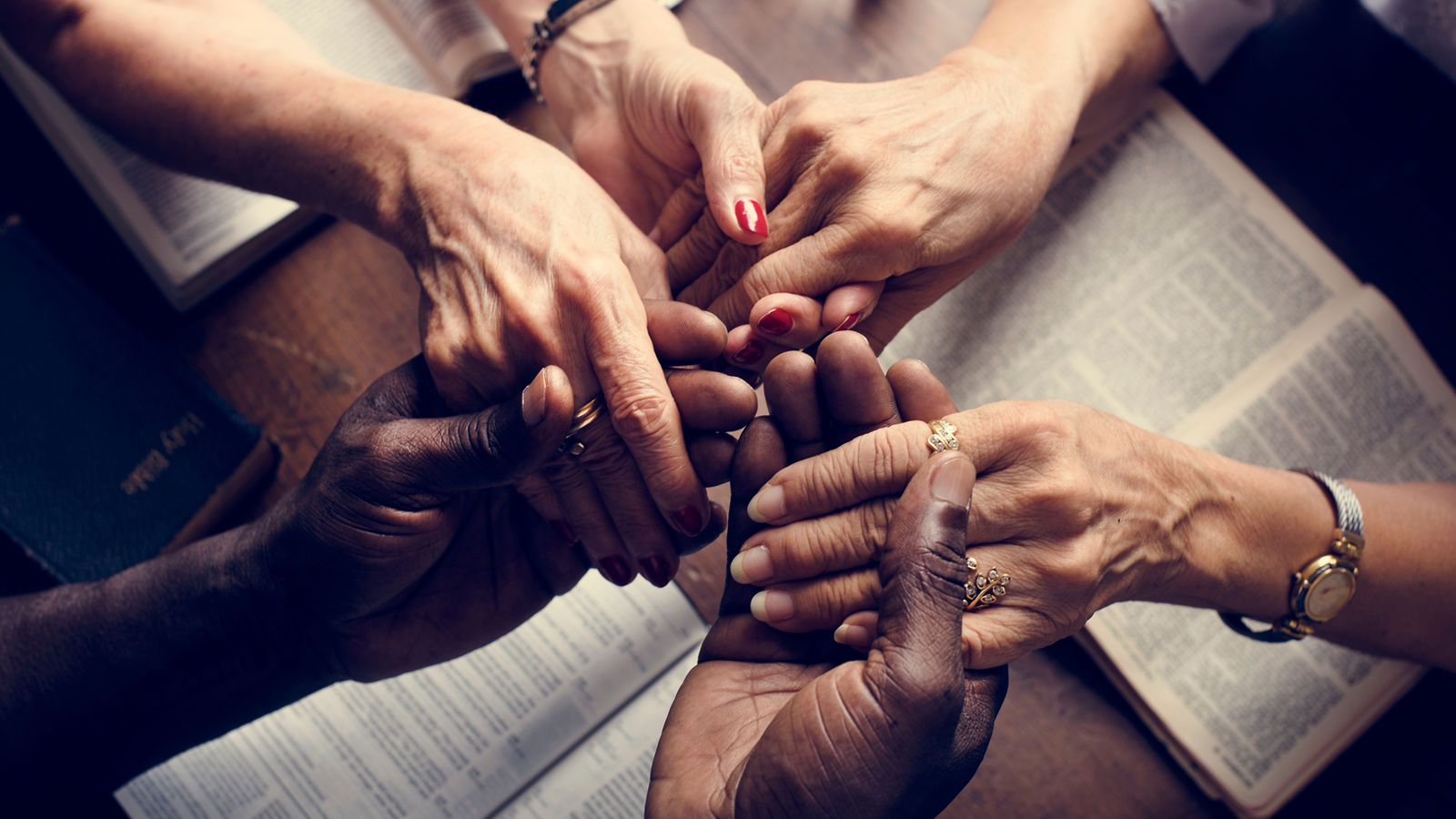 Several pairs of hands joined together over open Bibles.