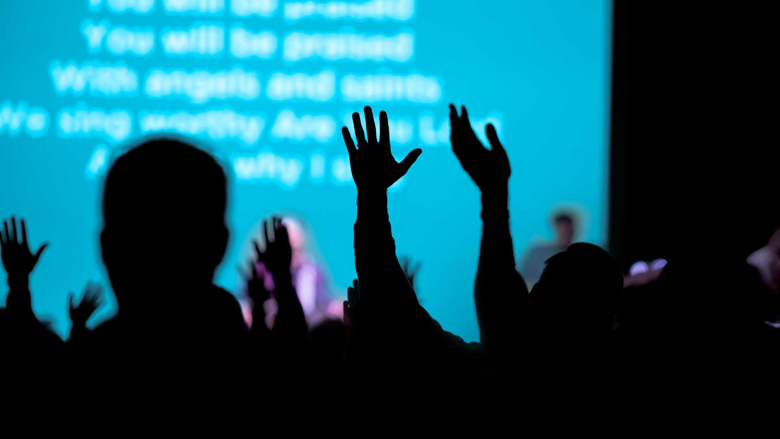Hands raised during a service, with the song words projected on the screen behind.